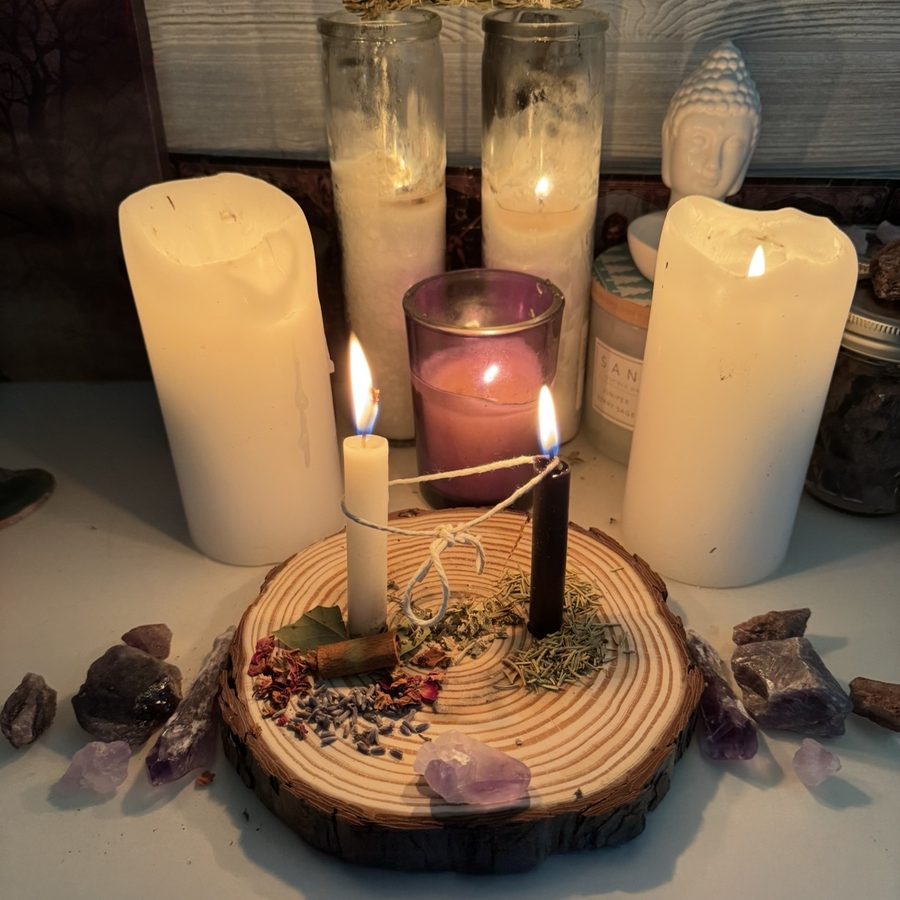 A cord cutting altar: lit candles, herbs on a wood round, and amethyst