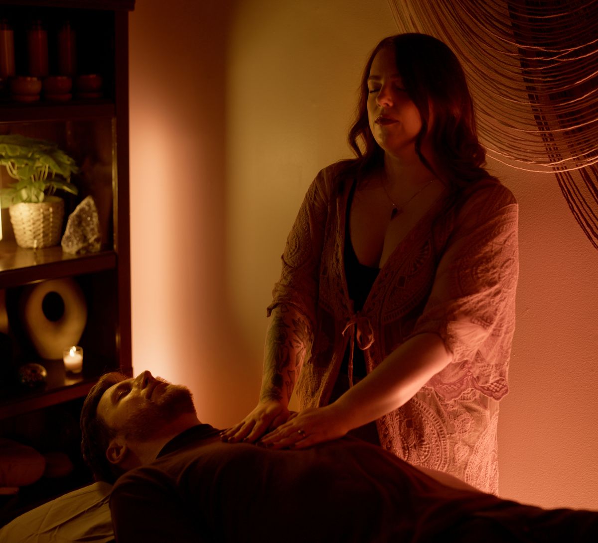 Alicia with her hands on a client's shoulders in the candlelit room